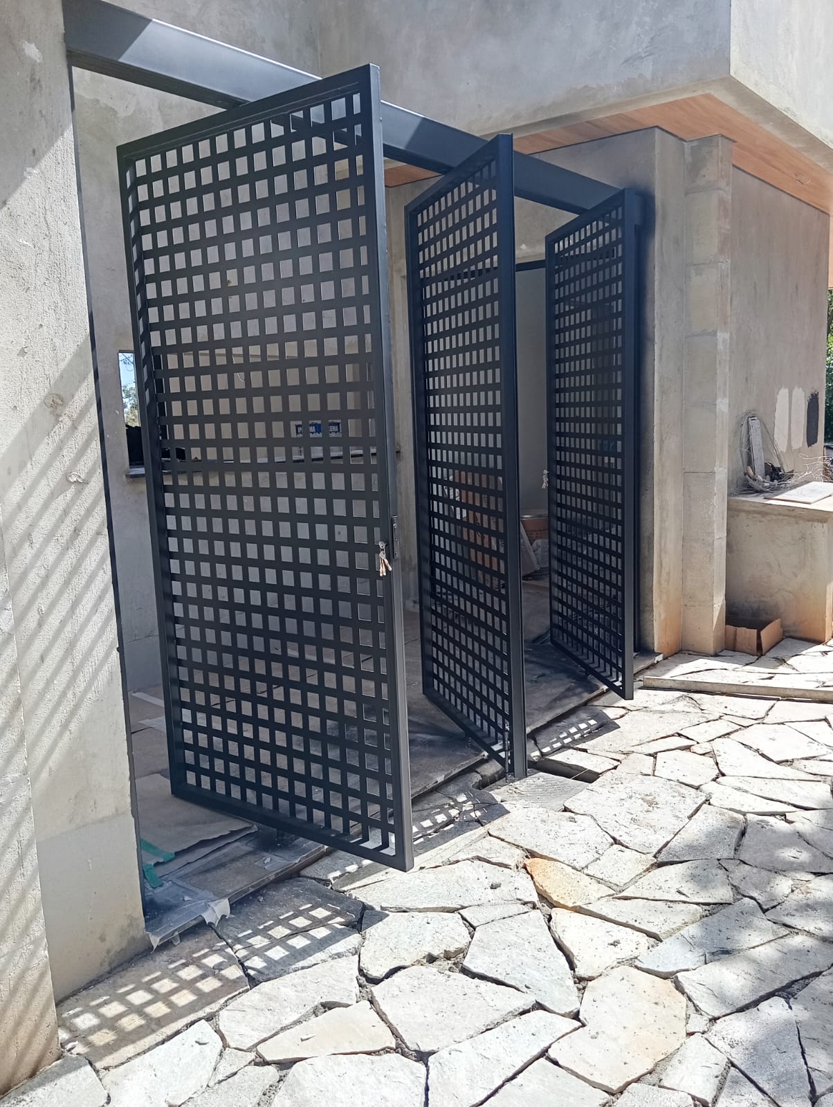 Portão com folhas abertas e recortes quadrados projetando sombras no piso